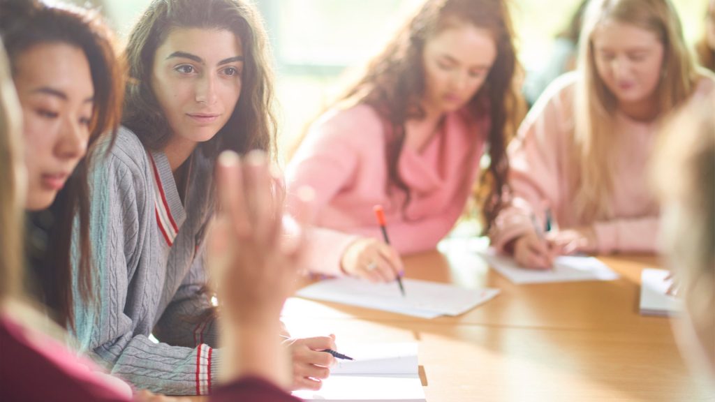 A small group of students sit around a table discussing and writing