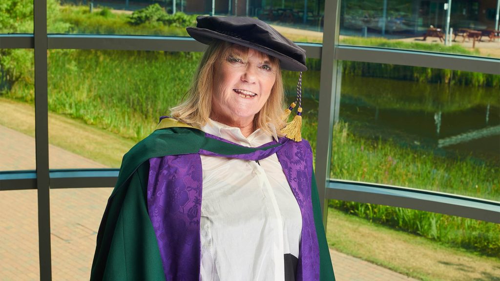 An image of Janice Long, there is a greenery behind.