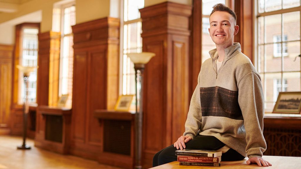 Student sitting on table in Sages with history books next to him