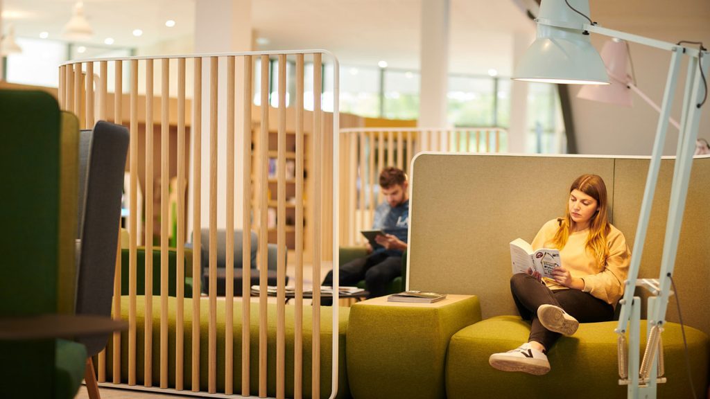 A student is reading a booking, sitting on green seating in the Catalyst