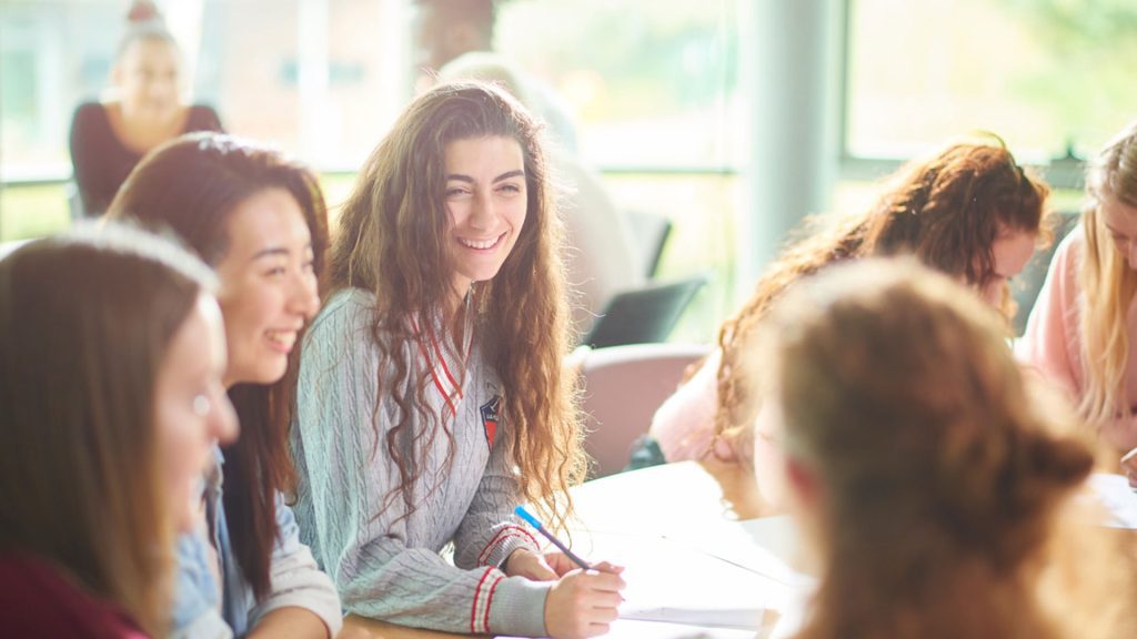 Four students sat together at a table whilst taking notes. They are laughing together.
