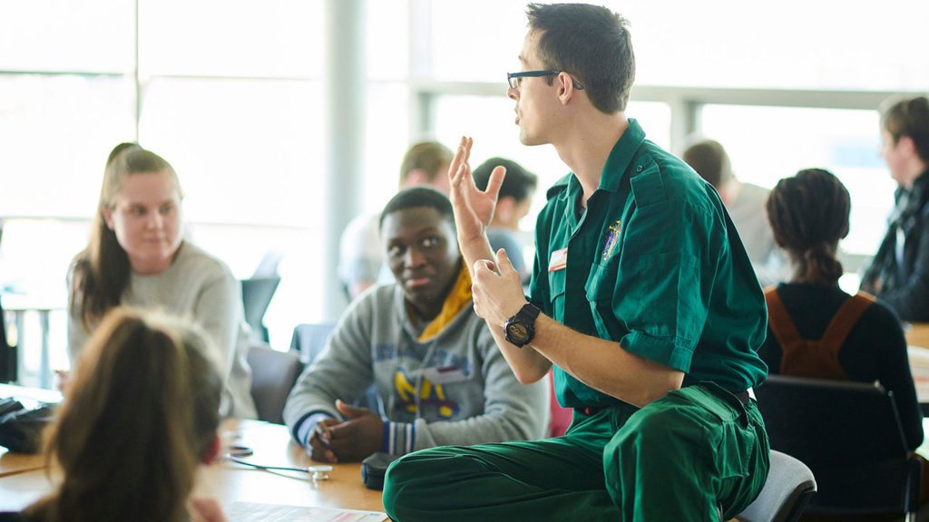 Widening access to medicine event. An Edge Hill medical representative talking to students at a desk.