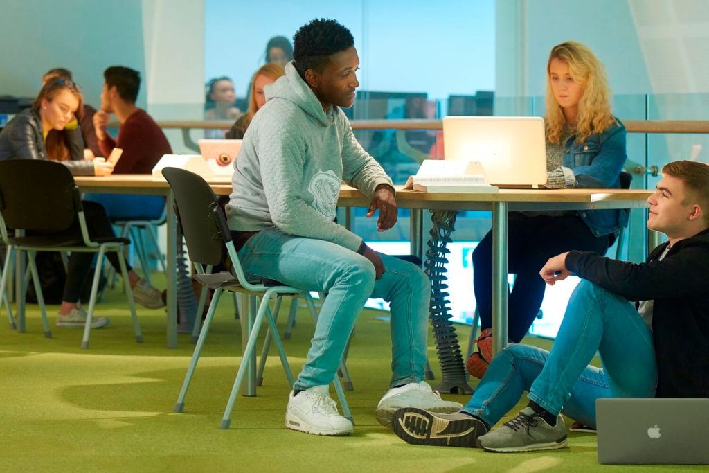 Students sit around tables in a social learning area on the first floor of the Tech Hub.