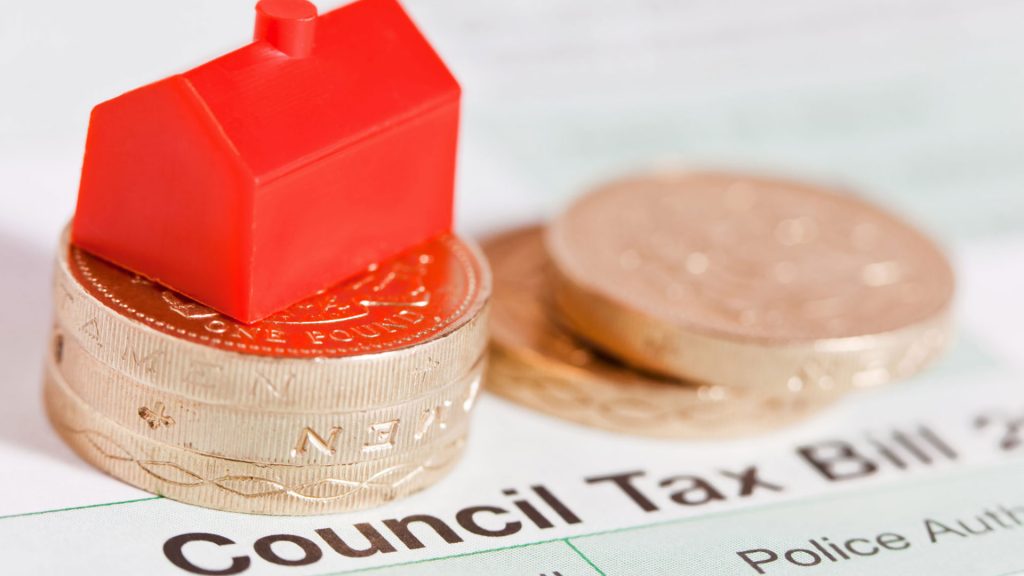 Paperwork for a council tax bill with some pound coins and a small red plastic toy house on top