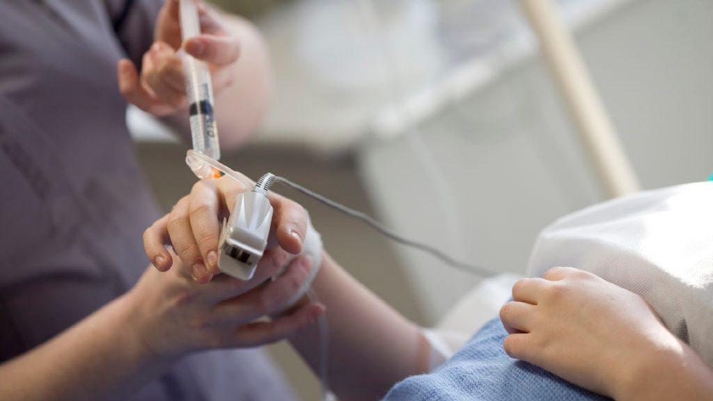 A student nurse is injecting something into a patient. There is a pulse oximeter on the finger of the patient.