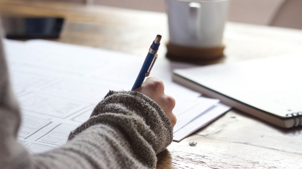 A persons hand writing on exam papers with a pen.