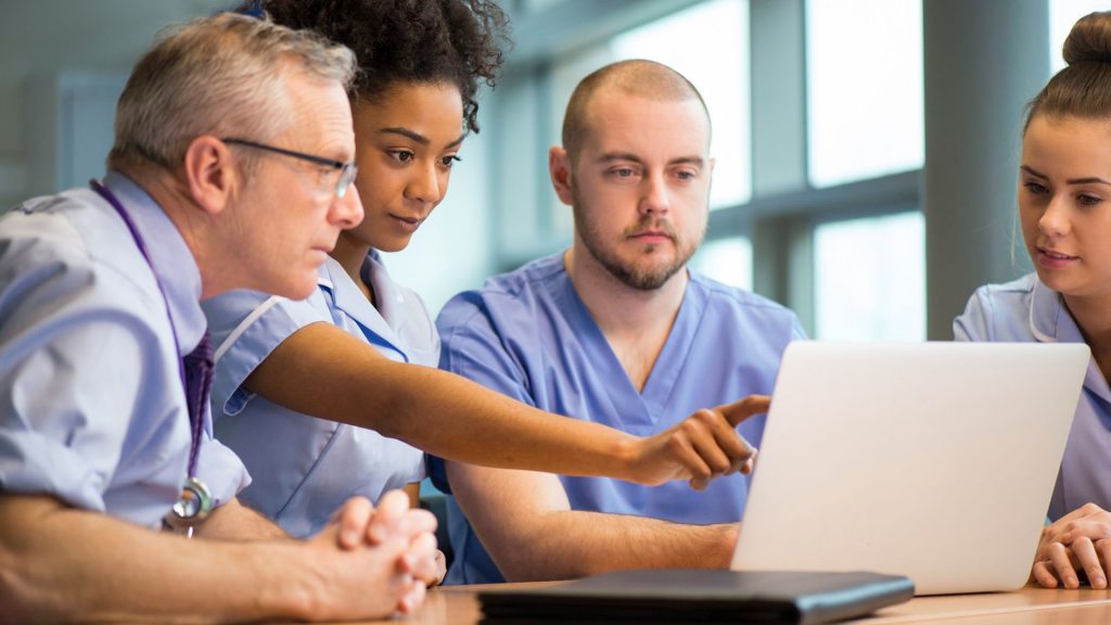 Three medical students and an academic are sat around a table together, looking at a laptop screen