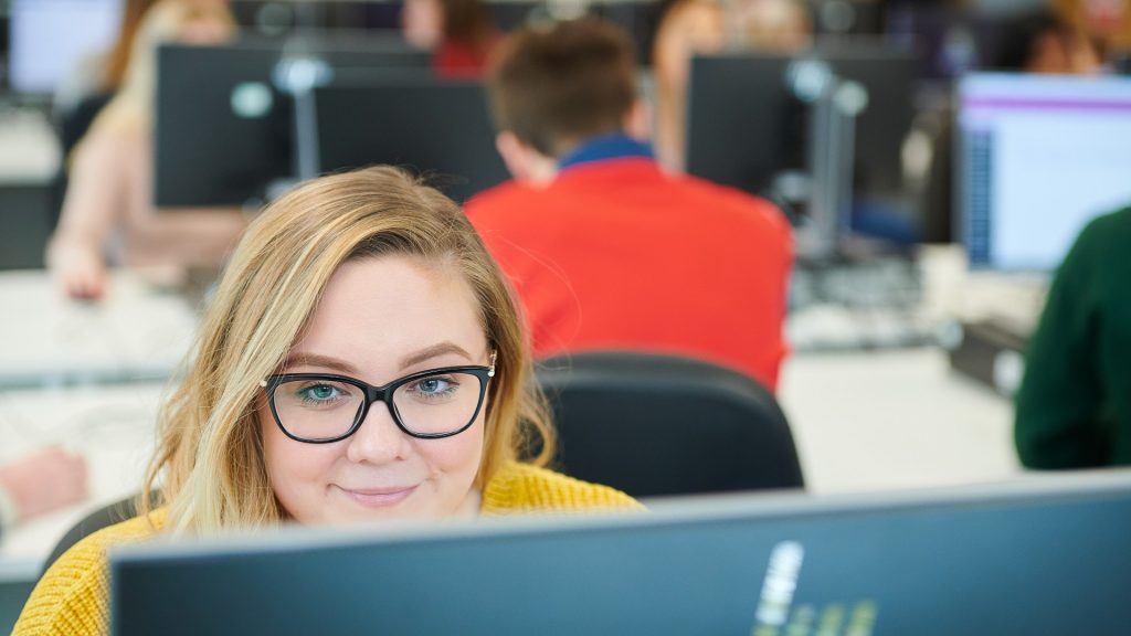 Student wearing glasses looking at monitor in computer room at Edge Hill