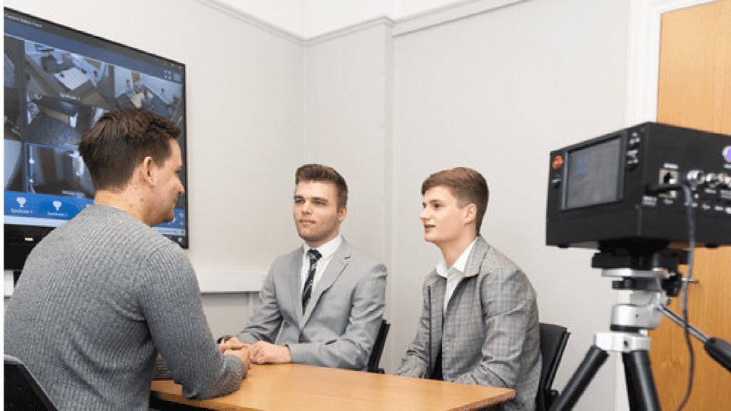 Three people are sat around a table, there is a camera pointing at them.