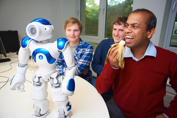 Dr Ardhendu Behera eats a banana next to Robbie the Robot