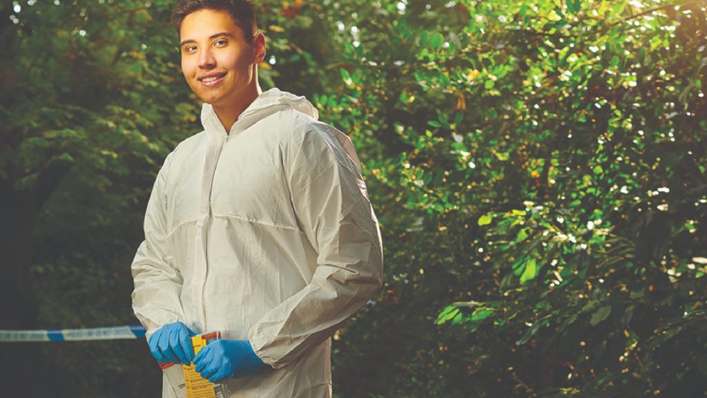 An image of a policing student stood behind caution tape. They are wearing a hazmat suit.