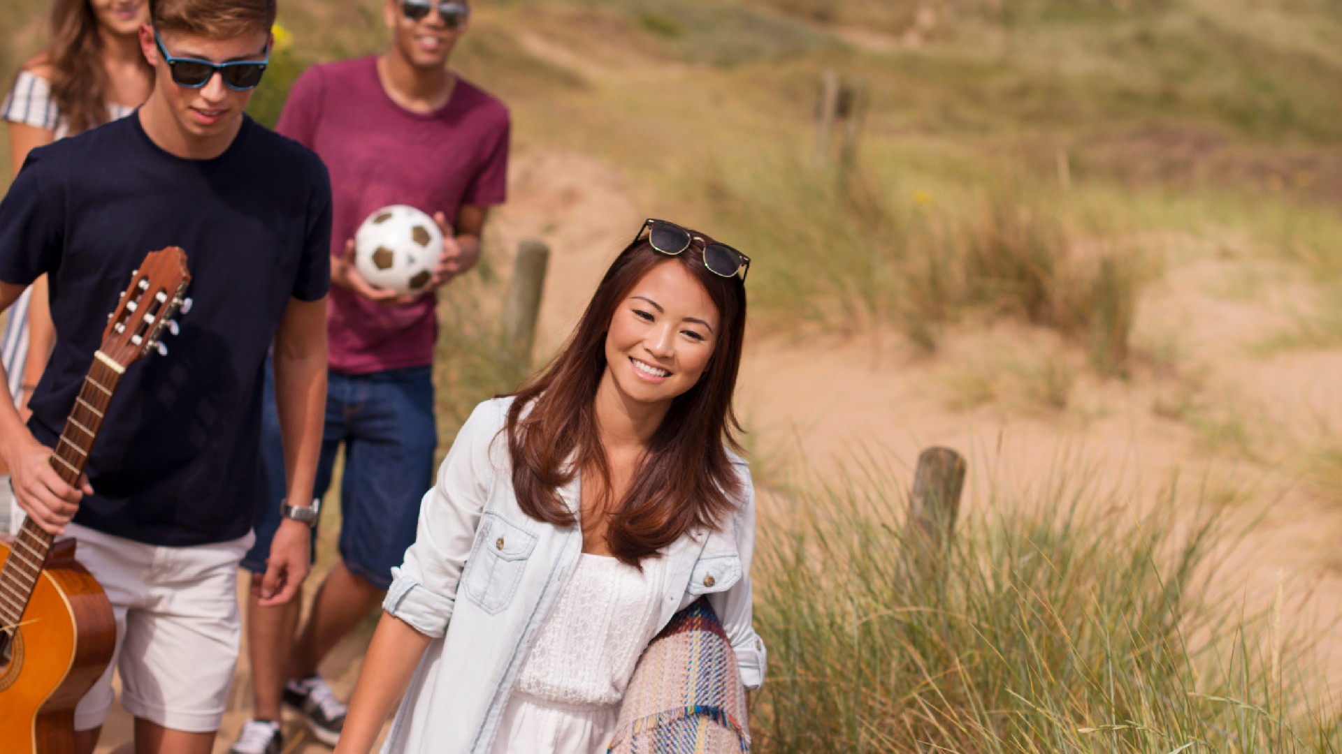 An image of people walking along Formby beach holding a guitar and a football. 