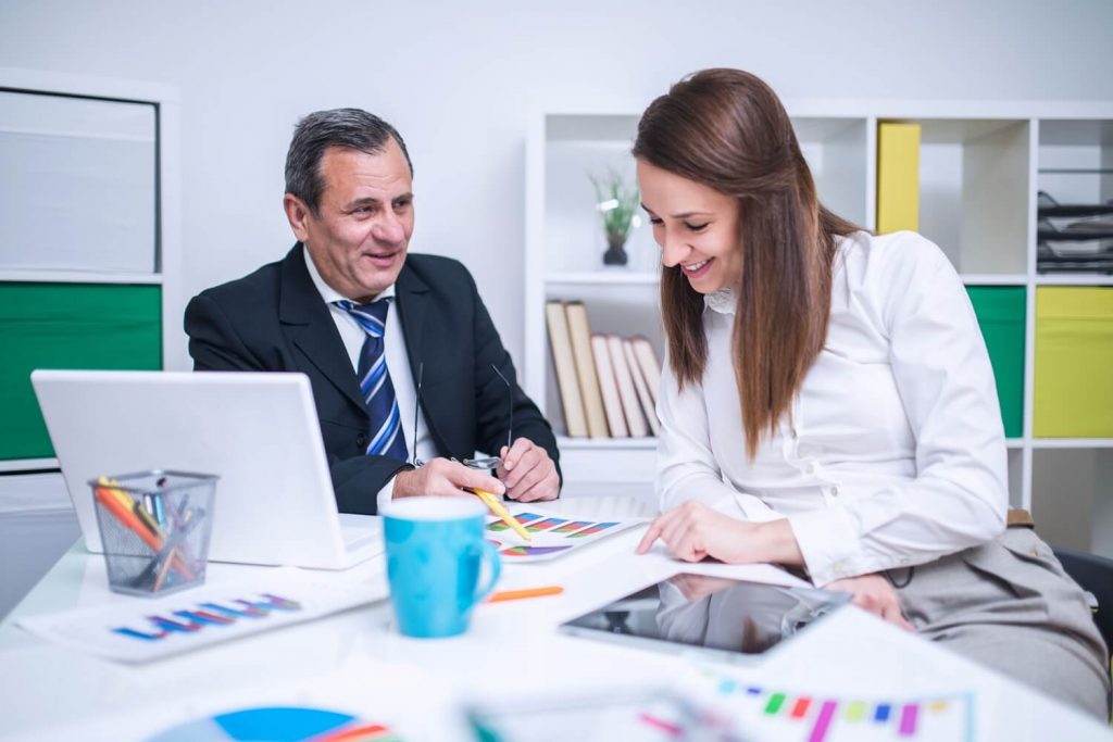 Two office workers study various charts while sat at a desk.