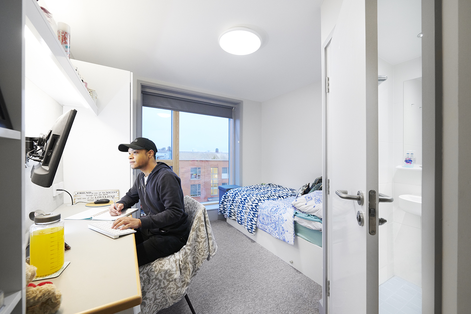 A students sits and writes at his desk in a bedroom in Woodland Court.