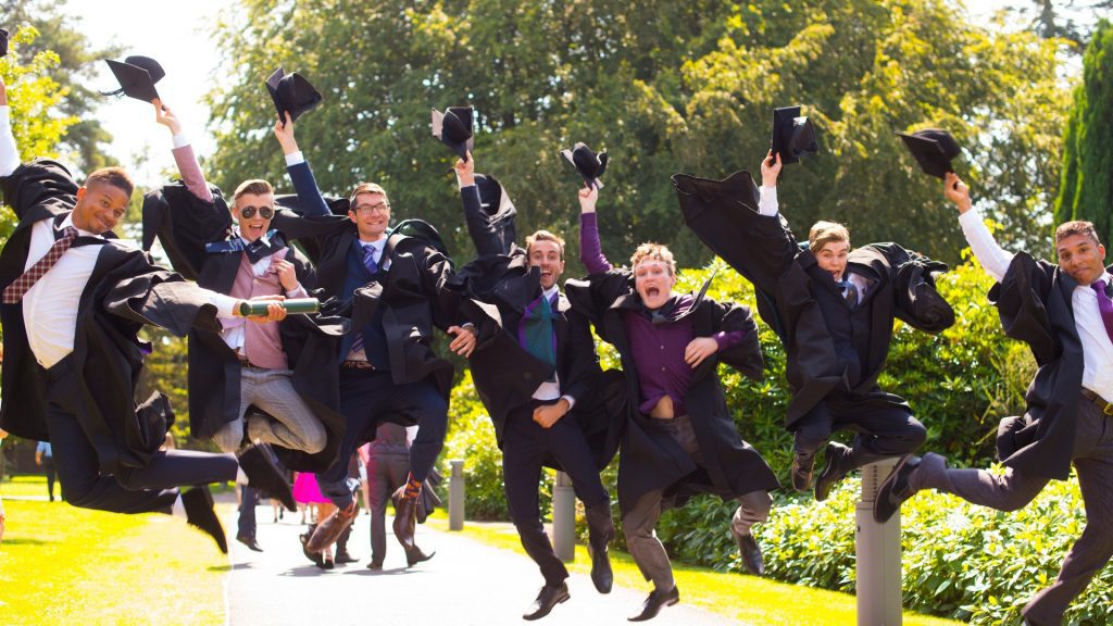 A group of people wearing graduation cap and gowns are jumping in the air.