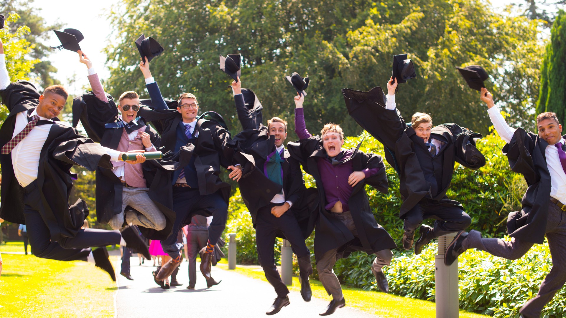 A group of people wearing graduation cap and gowns are jumping in the air.