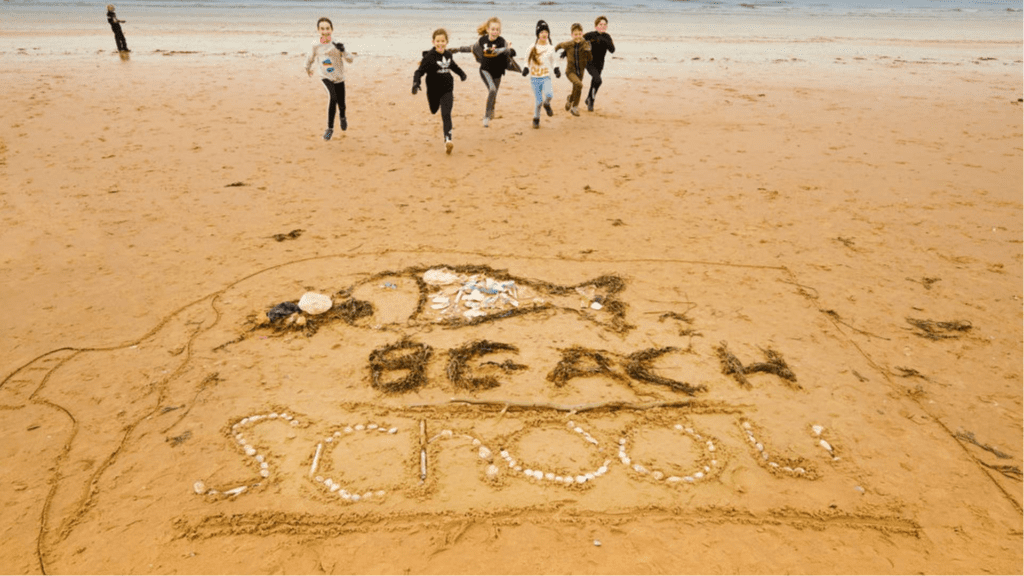An image of children running on the beach towards the words "Beach School" which are written in the sand.