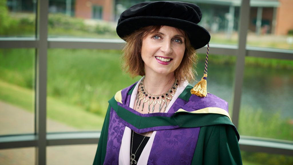 Sarah Niblock wearing green and purple robes for graduation.