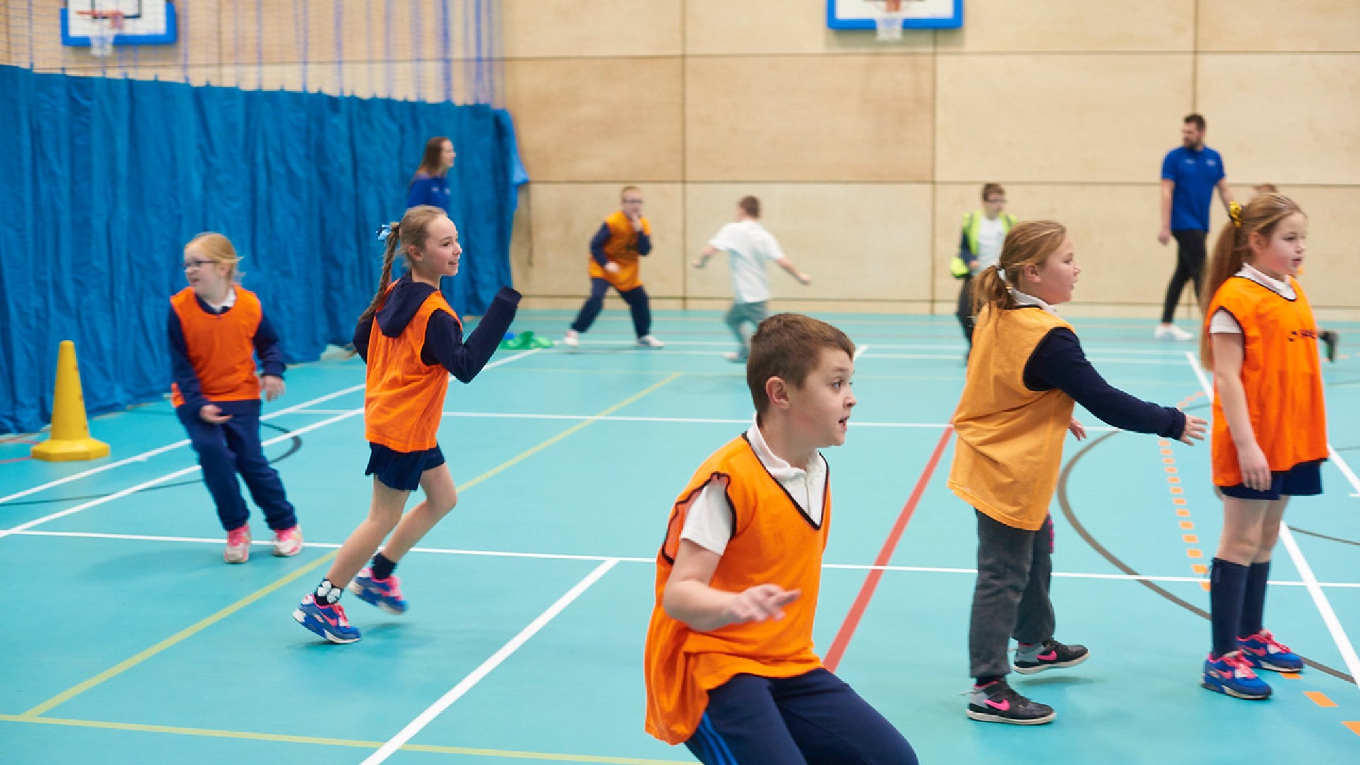 A group of children wearing orange vests are running around. 