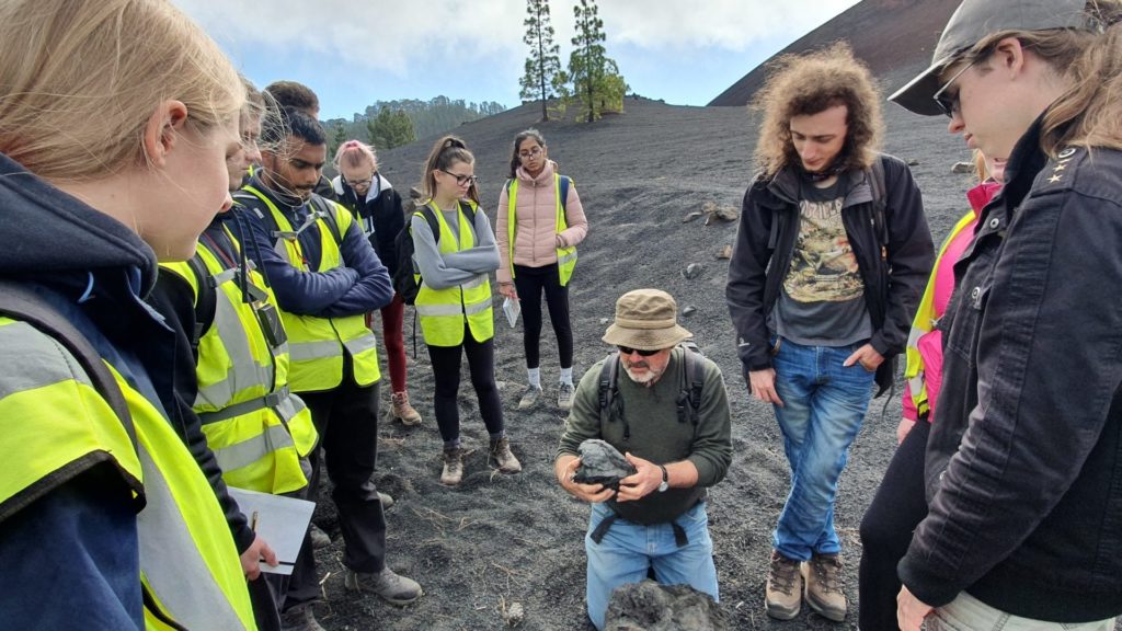 An image of a group of students, and a lecturer who is discussing a rock they are holding.