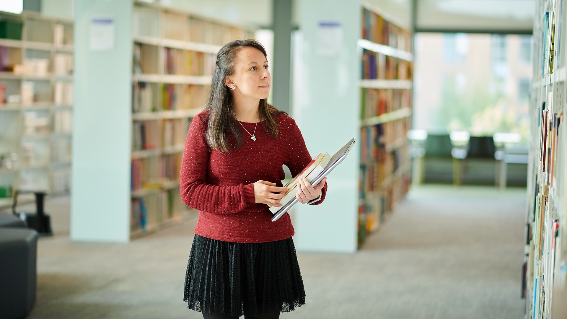 A student walking through the library with books in their hands