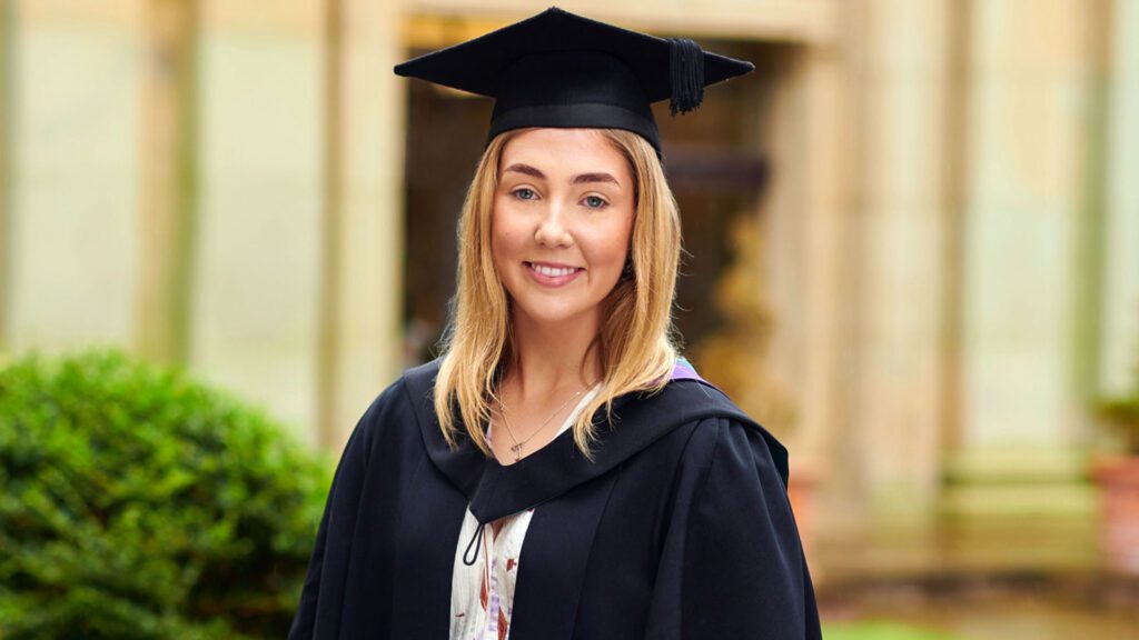 BSc (Hons) Marketing with Digital Communications alumni student, Jessica Barker, wearing a graduation cap an gown outside the Main building.