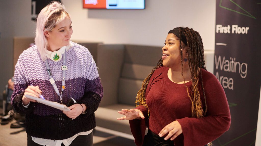 A careers advisor is stood up talking and smiling to a student