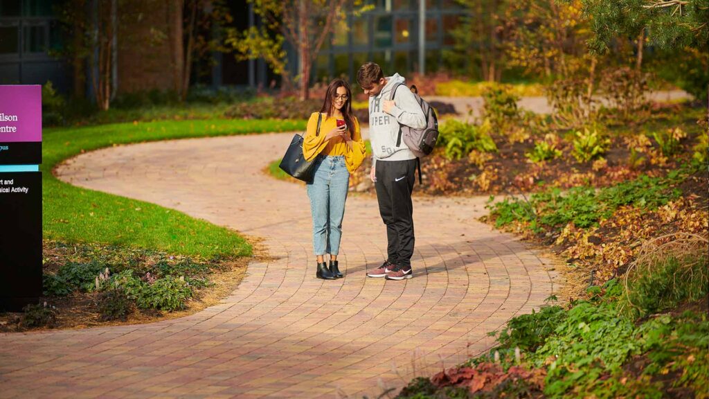 Two students looking at mobile phone on campus