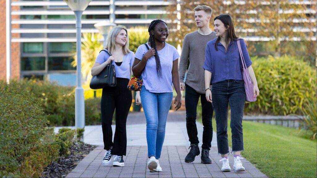 A group of students laugh and joke as they walk out of the main building