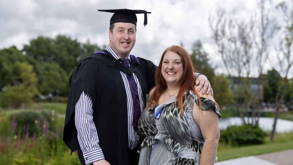 Andrew puts his around his wife Grace, they both smile at the camera.