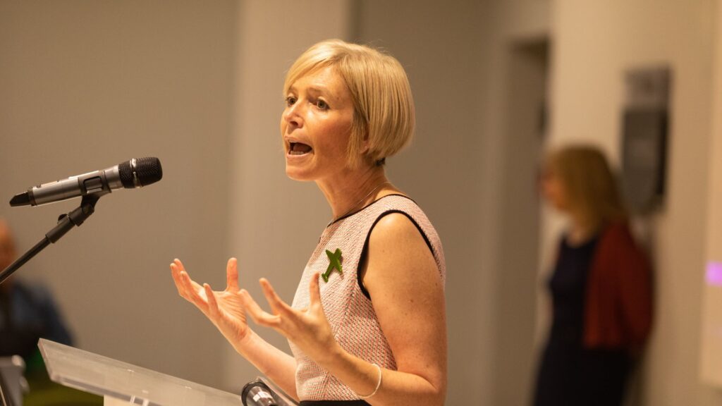Professor Jo Crotty stands behind a lectern and speaks into a microphone.