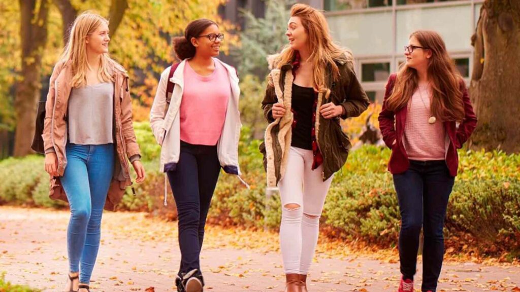 Four students walk past the Business School on an autumnal day.