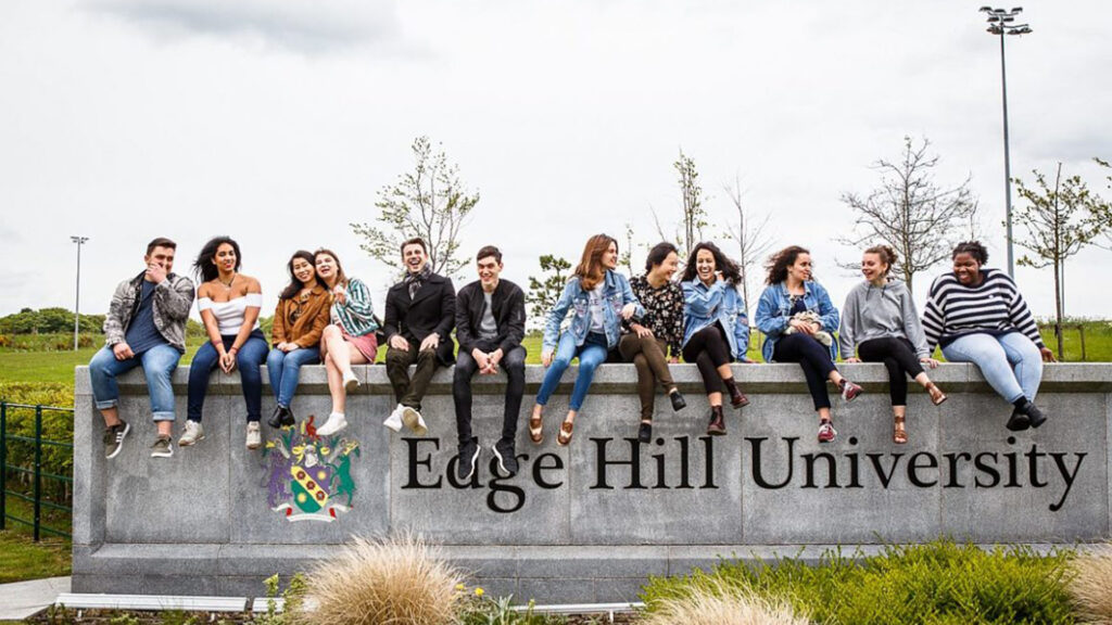 International students sit together on the Edge Hill University sign.