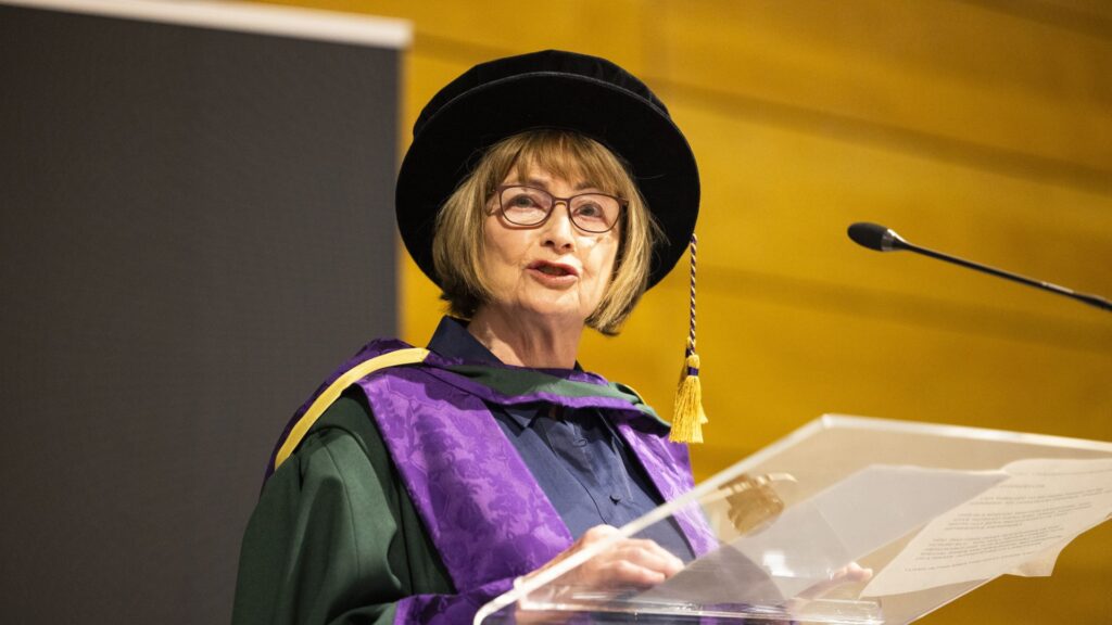 Dame Louise Ellman stands at a lectern and addresses the audience.