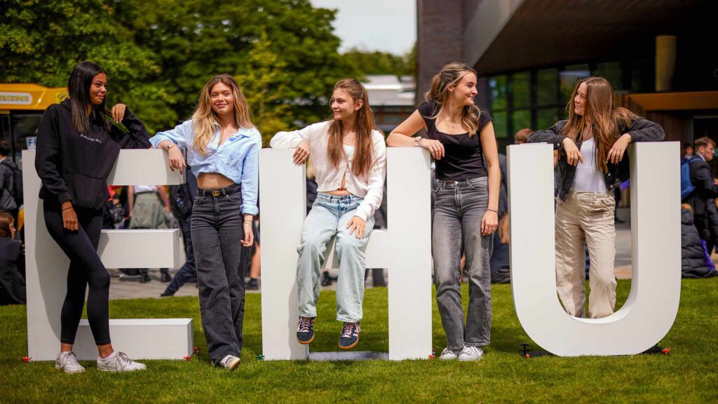 A group of college students exploring the campus on an open day, standing in front of the EHU letters