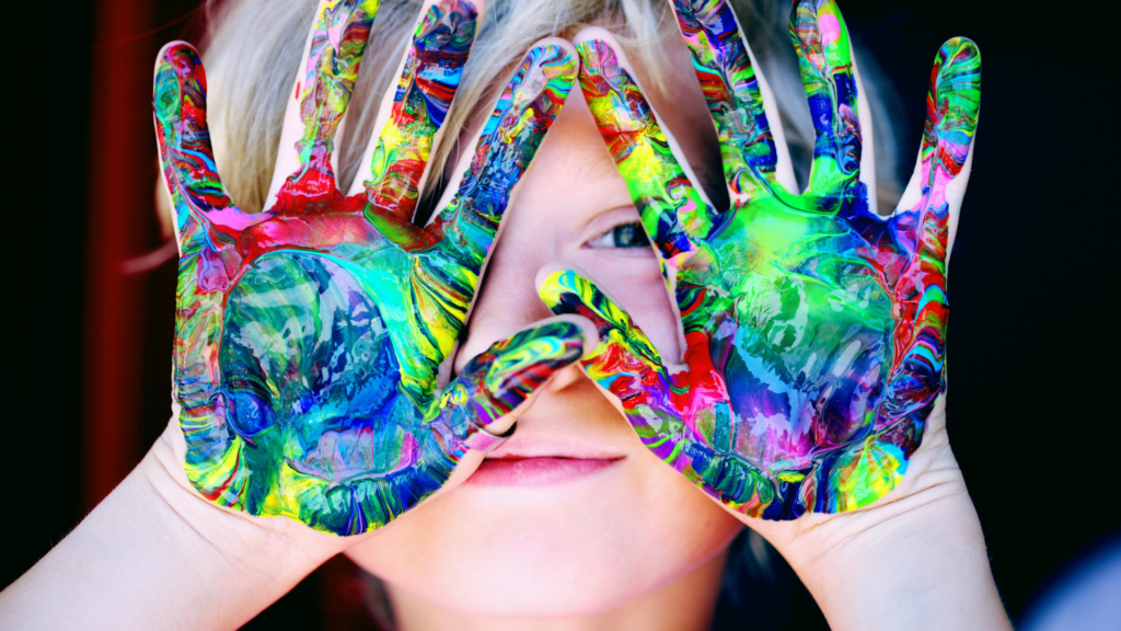 a young child with their hands covered in coloured paint