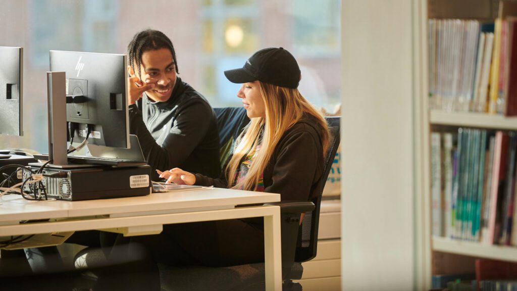 Two students talking while looking at something on the screen