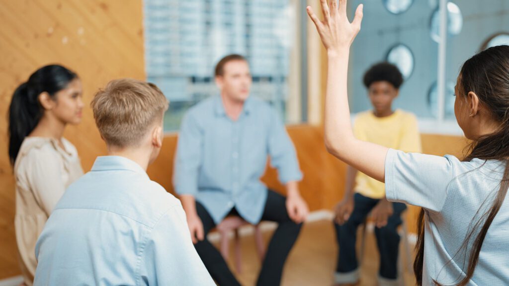 Adolescent children in discussion with lead and one child raising their hand to ask a question