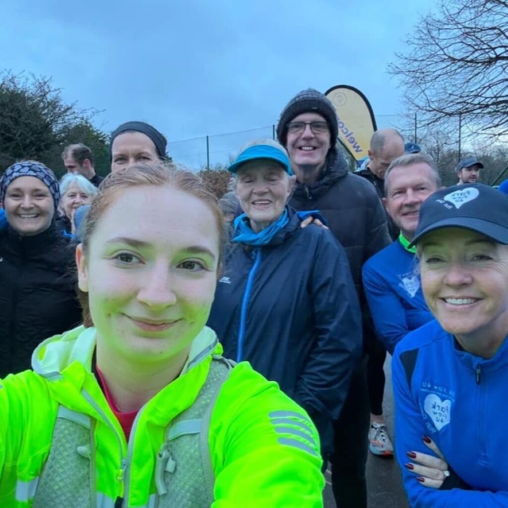 Zoe Harvey takes a selfie - she wears a high-vis jacket and is surrounded by people wearing blue sportswear.