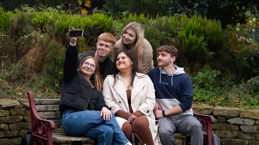 Students sitting on bench in town taking a picture together and smiling