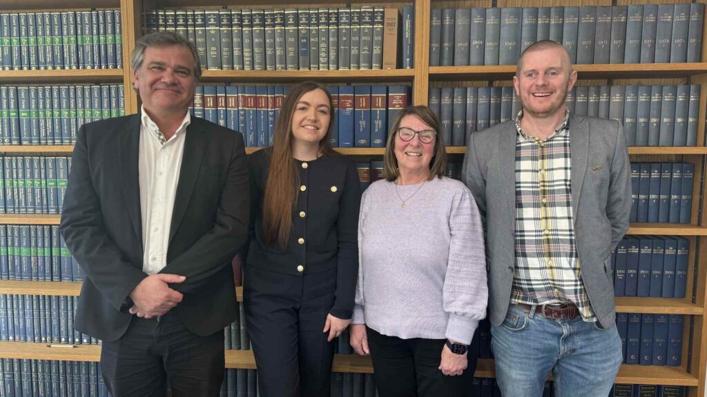 Managing Director Sarah Guilfoyle and Non-Executive Chair Brenda Spencer, Richard Parrish, Associate Head of the School of Law and Criminal Justice, & Senior Lecturer Adam Pendlebury. standing together in front of a shelf full of law books.
