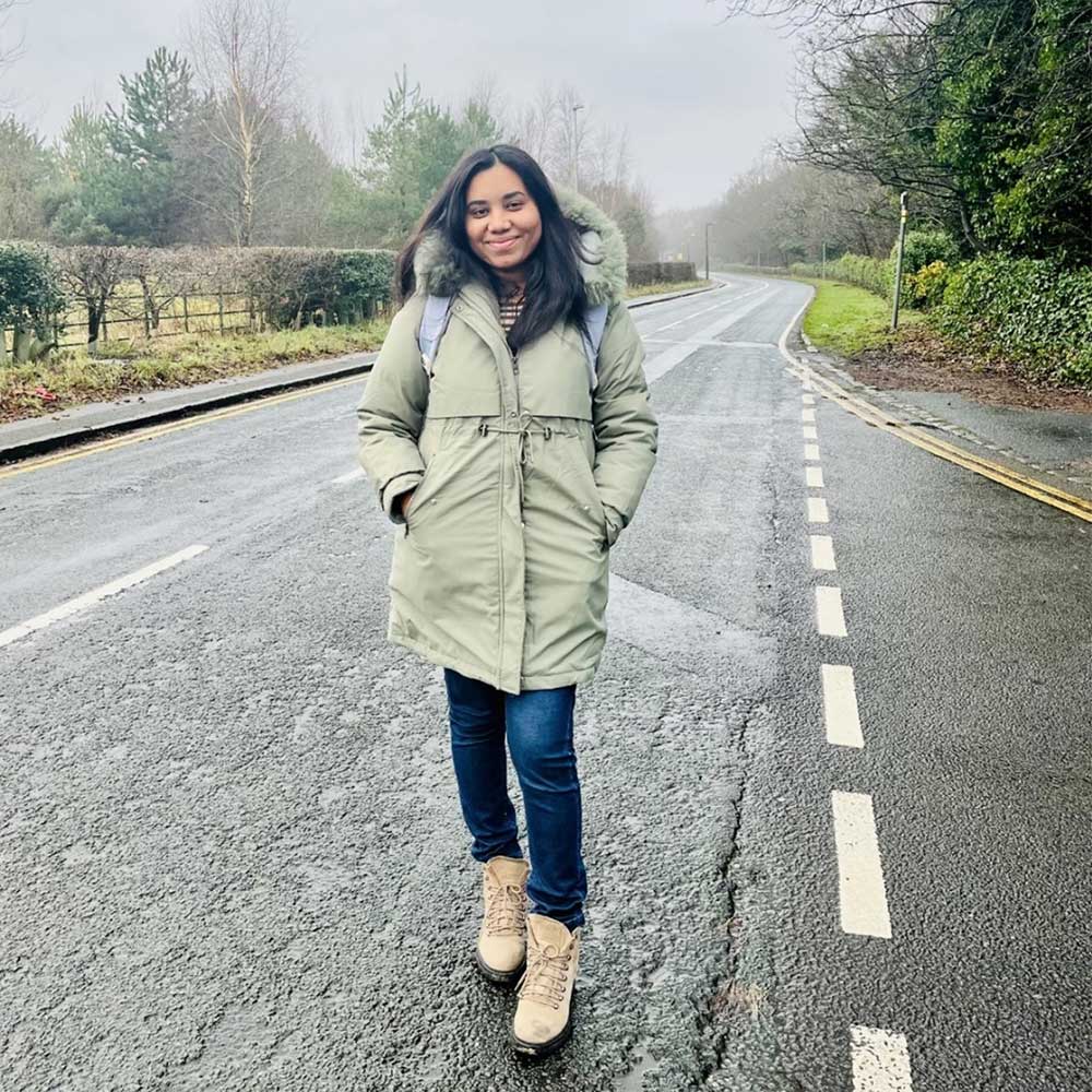 Shalini stood on a country road in a green parka jacket and wearing a backpack.
