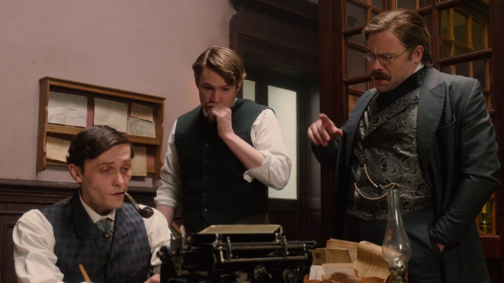 Three men dressed in 19th century clothes gather around a typewriter