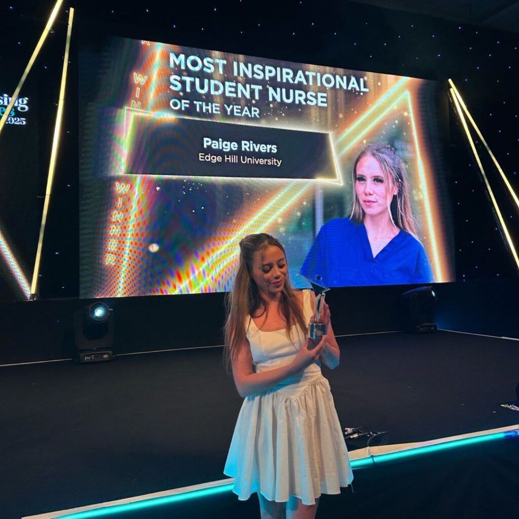 Paige wears evening dress and stands on a stage holding an award.