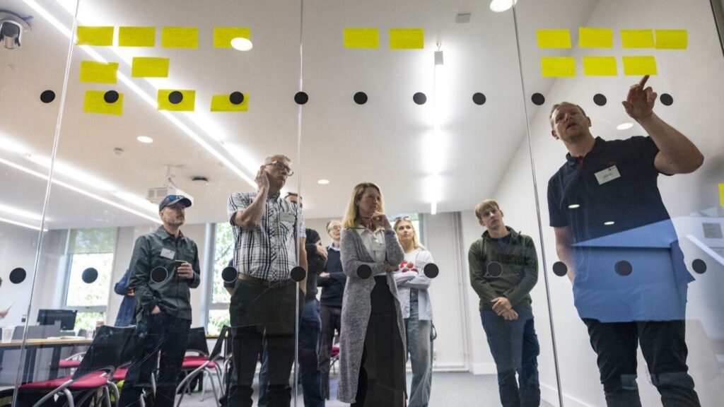 7 people standing in front of a glass wall with post stick notes all over them.