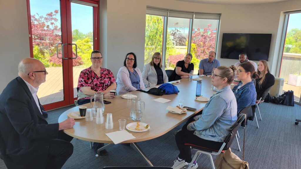 12 visitors from the University of Toledo sitting in a board room listening to staff male leader from Edge Hill University