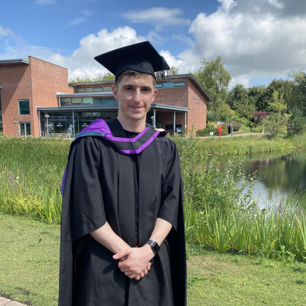 Student Darol Okane, standing outside EHU lake with graduation gown on