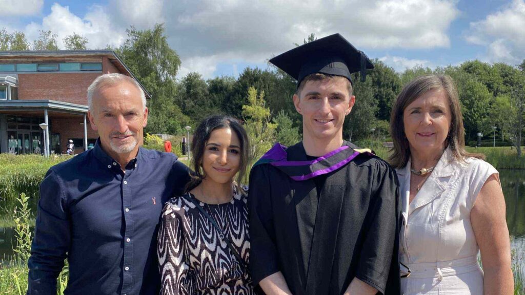 Student Darol Okane with mum, dad and fiancé outside EHU lake at graduation.