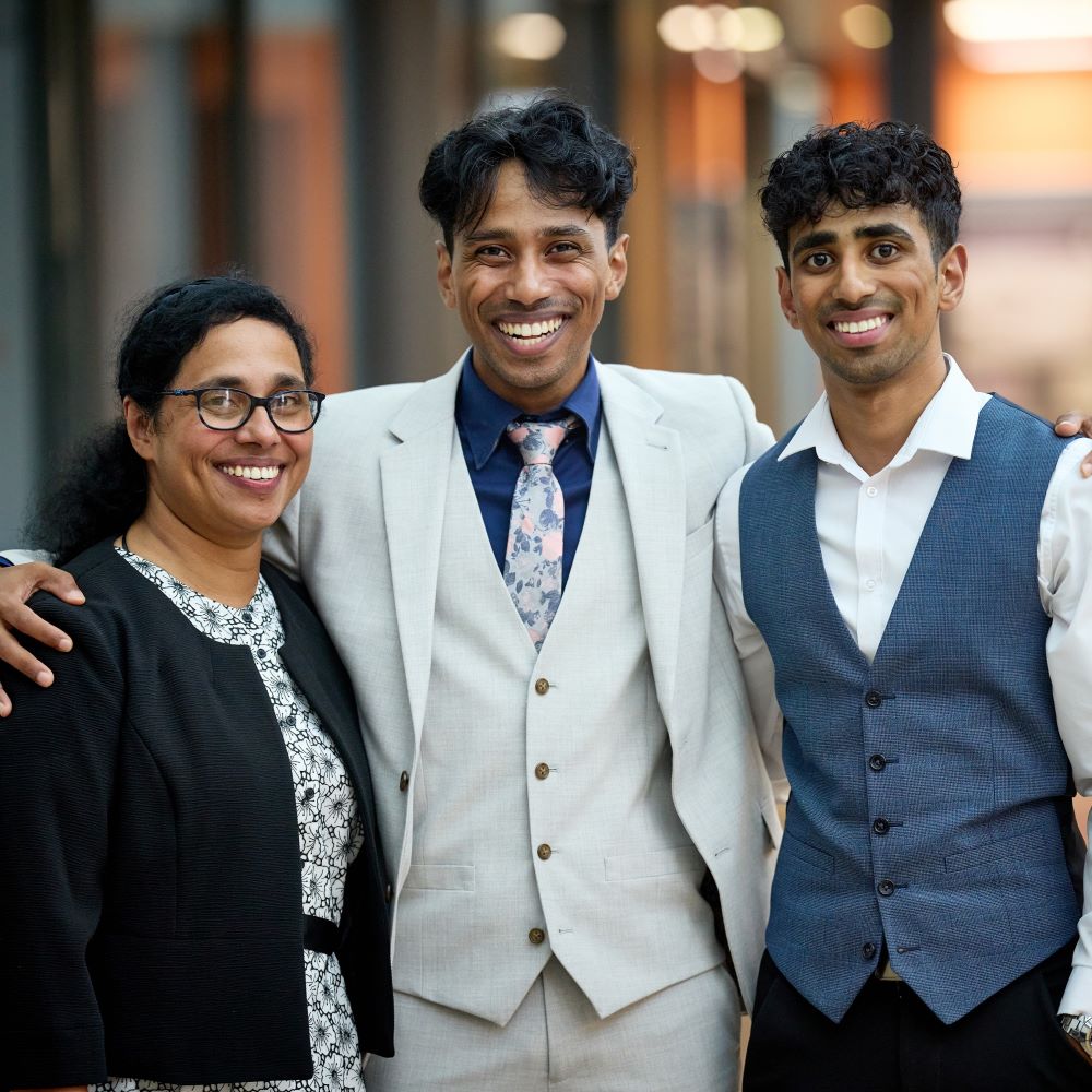 Glen stands in the middle with an arm round his mum on one side and his brother on the other. All three have big smiles on their faces.