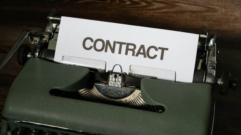 An old green typewriter. On the sheet of paper in there is the word 'contract' in large black font.